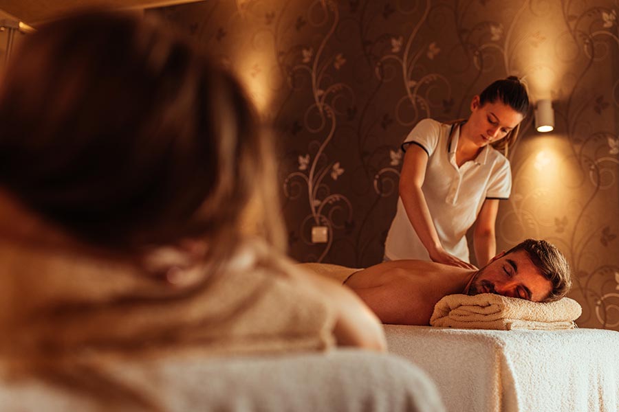 masseuse massaging male has he lays on massage table - photo is taken using the reflection of a wall mirror