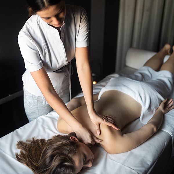 masseuse massaging lady 's shoulders as she lays on a bed